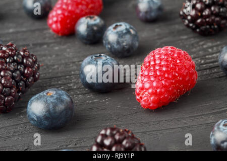 Bleuets frais, framboises et mûres sur fond de bois noir, selective focus. Banque D'Images