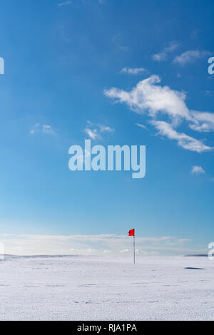 Golf rouge unique drapeau sur un désert vert couvert de neige sur un lumineux jour hivers contre un ciel bleu. Cleeve Hill, dans la région des Cotswolds, Gloucester, Royaume-Uni Banque D'Images