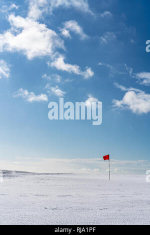 Golf rouge unique drapeau sur un désert vert couvert de neige sur un lumineux jour hivers contre un ciel bleu. Cleeve Hill, dans la région des Cotswolds, Gloucester, Royaume-Uni Banque D'Images