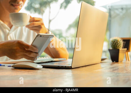 Hommes d'utilisation de téléphones cellulaires et de l'écriture sur ordinateur portable avec stylo sur table. Banque D'Images