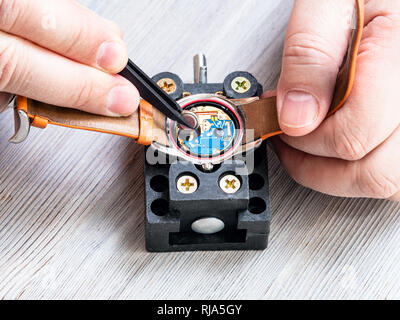Atelier de réparateur watch - vue avant d'horloger du remplacement de la batterie dans la montre-bracelet à quartz avec des pinces en plastique sur la table en bois close up Banque D'Images
