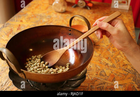 La main de femme à l'aide d'une pelle en bois brut de la torréfaction des grains de café dans une casserole en cuivre pour le café fait maison Banque D'Images