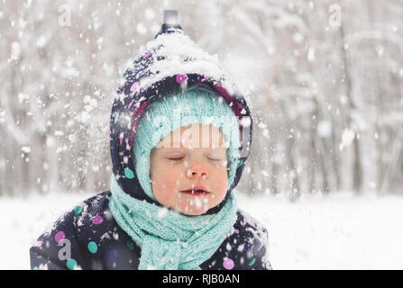 Bébé dans un pyjama d'hiver se réjouit dans la première neige Banque D'Images