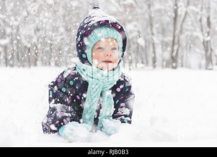 Bébé dans un pyjama d'hiver se réjouit dans la première neige Banque D'Images