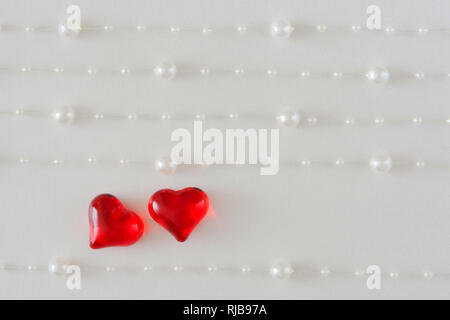 Fond de carte de mariage, la Saint Valentin avec deux coeurs brillants sur un fond blanc avec cinq cordes de perles blanches Banque D'Images