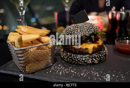 Noir savoureux burger, frites dans le panier et le ketchup servi sur noir planche à découper. Copier-collé du pavillon de l'espace en bun pour votre texte. Banque D'Images