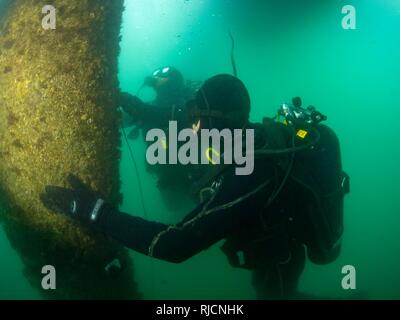 La construction de la Marine américaine 3e classe Mécanicien Lucan Jackson et de la Marine électricien de construction 2e classe Timothy Dailey, tous deux assignés à l'équipe de construction sous-marine (2) de l'UCT, enrouler une bande de coupe explosive (ECT) autour d'une pile au cours d'une plongée à Commandant, activités liées à la flotte de Sasebo (SCFA), Japon, le 16 janvier 2018. UCT-2 prévoit la construction, l'inspection, l'entretien, et la réparation des installations sous-marines et le bord de l'eau à l'appui de la Flotte du Pacifique. Banque D'Images