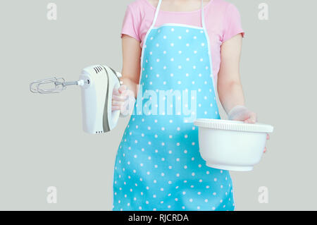 La fille dans le tablier de cuisine est la tenue d'une table de mixage et un bol. Fond gris. Banque D'Images