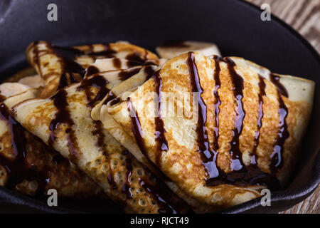 Des crêpes faites maison avec la banane et chocolat topping pour le petit-déjeuner dans la poêle en fonte sur table en bois rustique, Close up, selective focus Banque D'Images