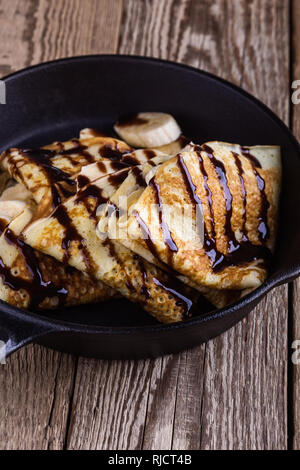 Des crêpes faites maison avec la banane et chocolat topping pour le petit-déjeuner dans la poêle en fonte sur table en bois rustique, Close up, selective focus Banque D'Images