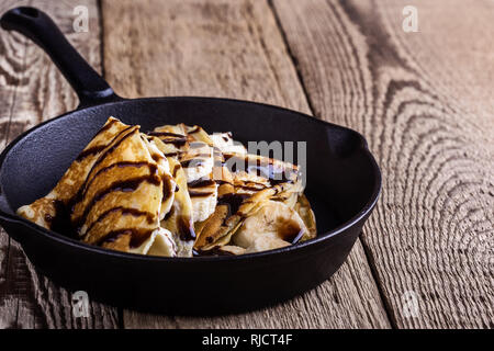 Des crêpes faites maison avec la banane et chocolat topping pour le petit-déjeuner dans la poêle en fonte sur table en bois rustique, Close up, selective focus Banque D'Images