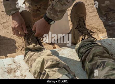 Un soldat de l'Armée américaine affecté à la Force opérationnelle interarmées - Corne de l'Afrique se desserre les bottes d'une chaleur simulée victime durant la formation pour un expert Infantryman Badge (BEI) Évaluation au Camp Lemonnier, Djibouti, le 23 janvier 2018. La BEI est une des compétences particulières d'un insigne qui exige de l'infanterie à passer cinq jours d'évaluation qui se compose d'un test de condition physique de l'armée, jour et nuit, la navigation terrestre, une marche forcée de 12 km, et 30 tâches individuelles couvrant les armes, medical, patrouille de sécurité et de compétences. En avril 2016 une itération de la BEI au Camp Lemonnier, seulement 15 pour cent des candidats ear Banque D'Images