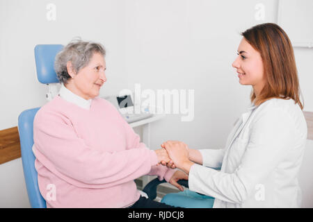 Friendly doctor shaking âgés de woman's hand in office Banque D'Images