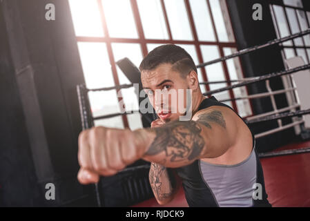 Athlète musculaire très fort dans les vêtements de sport pratique droit de poing droit dans la boxe de fitness. Confiant de faire boxer-ombres près de ring de boxe boxe Banque D'Images