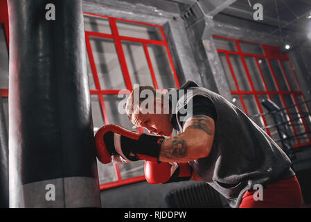 Confiant en rouge sportif musculaire gants de sport exercice sur sac lourd. Formation dur sur fond de sport boxe Banque D'Images