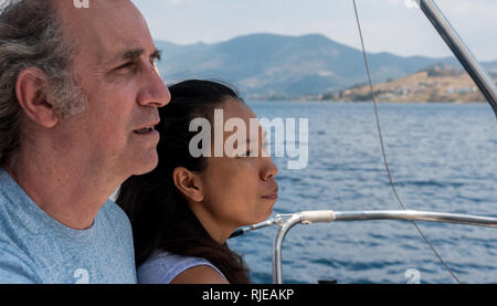 Libre de l'homme et de la femme dans le cockpit d'un voilier avec les montagnes et la mer en arrière-plan Banque D'Images