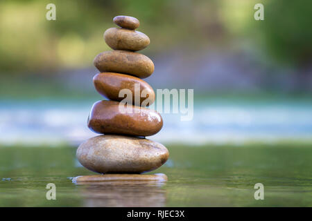 Close-up image abstraite de brun naturel rugueux humides de différentes tailles et formes irrégulières équilibré pyramide pierres comme monument de pieux dans l'eau peu profonde sur blu Banque D'Images