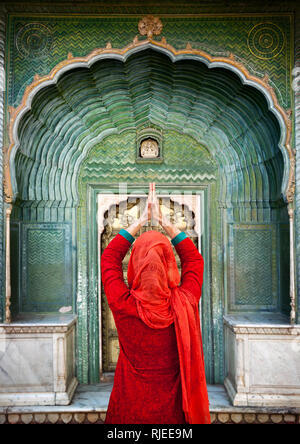Femme indienne en écharpe rouge avec mains en prière au geste green gate porte, dans les palais de la ville de Jaipur, Rajasthan, Inde. L'espace pour votre texte, peuvent être utilisés Banque D'Images