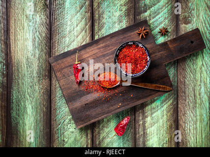 Paprika en poudre et piment rouge foncé sur une planche à découper à table en bois vert Banque D'Images
