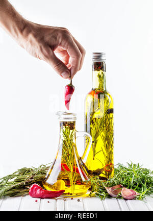 Man putting red chili pepper dans la bouteille avec de l'huile, les herbes et épices sur fond blanc Banque D'Images