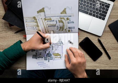 Vue de dessus du mans mains dessin dans l'album sur la table en bois à côté d'ordinateur portable et le smartphone Banque D'Images