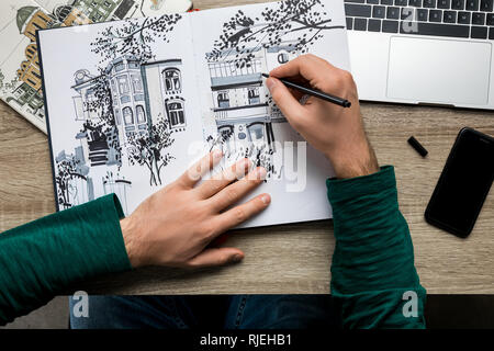 Vue de dessus du mans mains dessin dans l'album sur la table en bois à côté de l'ordinateur portable et smartphone Banque D'Images