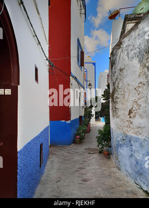 Rue étroite à l'intérieur de l'ancienne médina d'Asilah, Maroc ville : blanc vieux murs en pierre avec des portes rouges et bleues. Banque D'Images