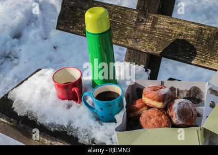 Thermos vert, rouge et bleu de tasses de café et fort avec donuts sur le banc en bois recouvert de neige sur le mont Kosmaj, près de Belgrade, Serbie Banque D'Images