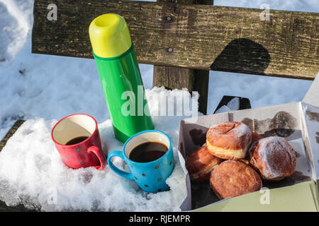 Thermos vert, rouge et bleu de tasses de café et fort avec donuts sur le banc en bois recouvert de neige sur le mont Kosmaj, près de Belgrade, Serbie Banque D'Images