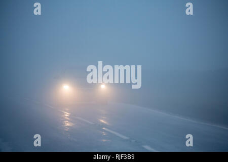 Une voiture avec ses phares sur conduire lentement dans un épais brouillard dans l'après-midi en février. Nord du Dorset England UK GO Banque D'Images