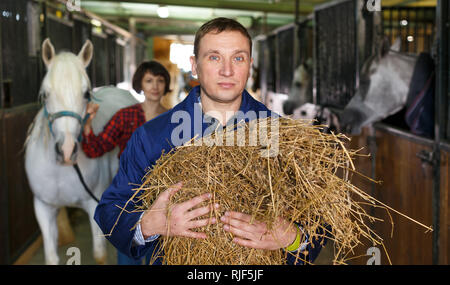 Homme travailleur agricole à l'alimentation avec du foin à stable Banque D'Images