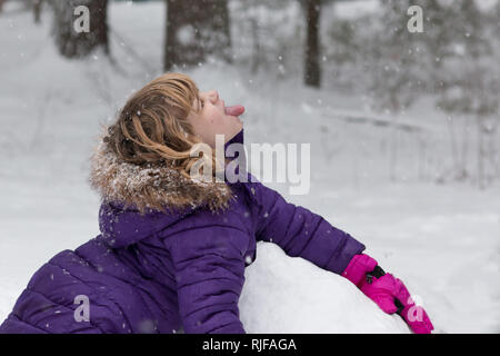 Une fillette de 8 ans jouer dans la neige colle dehors sa langue pour attraper des flocons de neige. Banque D'Images