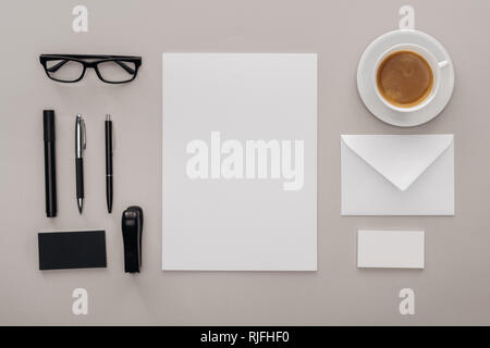 Mise à plat avec lunettes noires, papeterie et cartes blanc vide sur le lieu de travail avec une tasse de café sur fond gris Banque D'Images