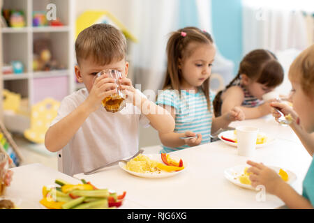 Déjeuner dans la garderie. Groupe d'enfants mangent des aliments sains. Kid boy boire du jus pendant le dîner dans le jardin d'enfants Banque D'Images