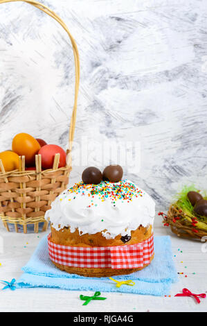 Gâteau traditionnel de Pâques - kulich, des œufs en chocolat dans un nid, les oeufs peints et colorés sur un fond blanc en bois. Pain Décoré de meringue. À Banque D'Images