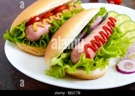 De savoureux hot dogs avec saucisses grill, ketchup, moutarde, laitue, tomates sur une assiette blanche. Close up Banque D'Images