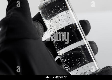 Portrait de femme en noir main gant avec bouteille cosmétique transparent sur fond blanc Banque D'Images