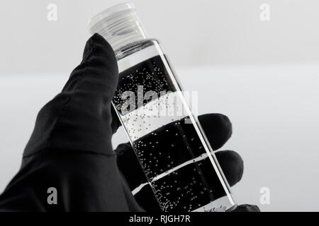 Portrait de femme en noir à la main avec un gant de bouteille avec un liquide transparent sur fond blanc Banque D'Images