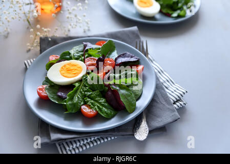 Mélange de salade aux épinards, roquette, feuilles de betterave, tomates et œufs sur fond de bois gris. Concept d'aliments végétariens. Focus sélectif. Banque D'Images