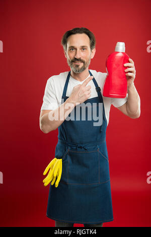 La garde de la propreté et l'ordre. Service de nettoyage et de service à la personne. L'homme à tenir avec des gants tablier bouteille plastique savon liquide de nettoyage chimique. Journée de nettoyage d'aujourd'hui. Accueil nettoyage barbu. Banque D'Images