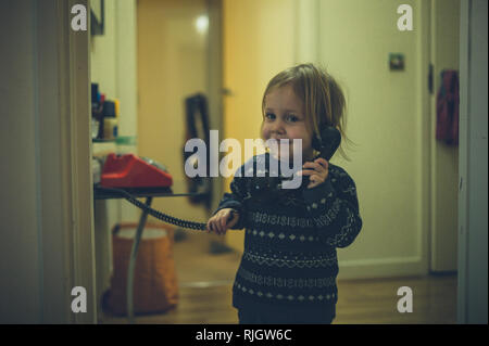 Un mignon petit bambin parle sur un vieux téléphone à cadran Banque D'Images