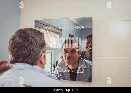 Un couple gay ensemble en face de la salle de bains miroir. Banque D'Images