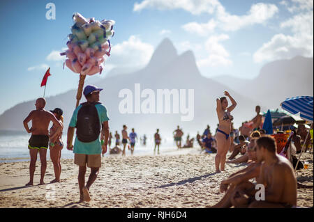 RIO DE JANEIRO - JANVIER, 2018 : Un vendeur de plage coton vente de la barbe à papa passe devant des clients potentiels sur la plage d'Ipanema. Banque D'Images