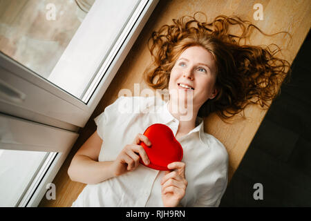 Belle jeune fille allongé par la fenêtre avec un cadeau pour la Saint-Valentin. Banque D'Images