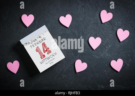 Calendrier de découpe avec 14 février (en allemand) sur le dessus, entouré de coeurs sur un fond d'ardoise Banque D'Images