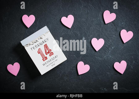 Calendrier de découpe entouré de coeurs avec 14 février sur le dessus sur un fond d'ardoise Banque D'Images