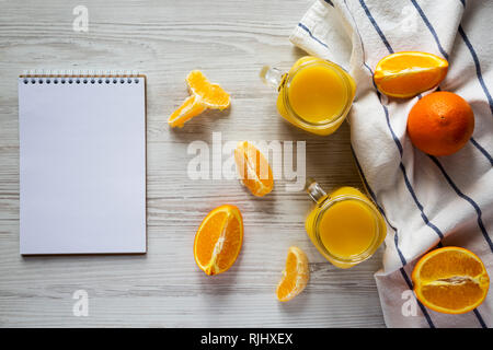 Jus d'orange dans des bocaux en verre, blank notepad over white background, vue de dessus. Mise à plat, d'en haut, vue d'en haut. Banque D'Images