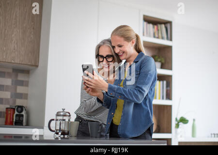 L'adulte femme avec grandi fille looking at smartphone in kitchen Banque D'Images