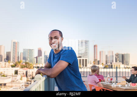 Portrait de jeune homme adulte à un rooftop party with city skyline Banque D'Images