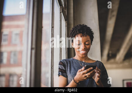 Young african american female in loft Appartement looking at smartphone Banque D'Images